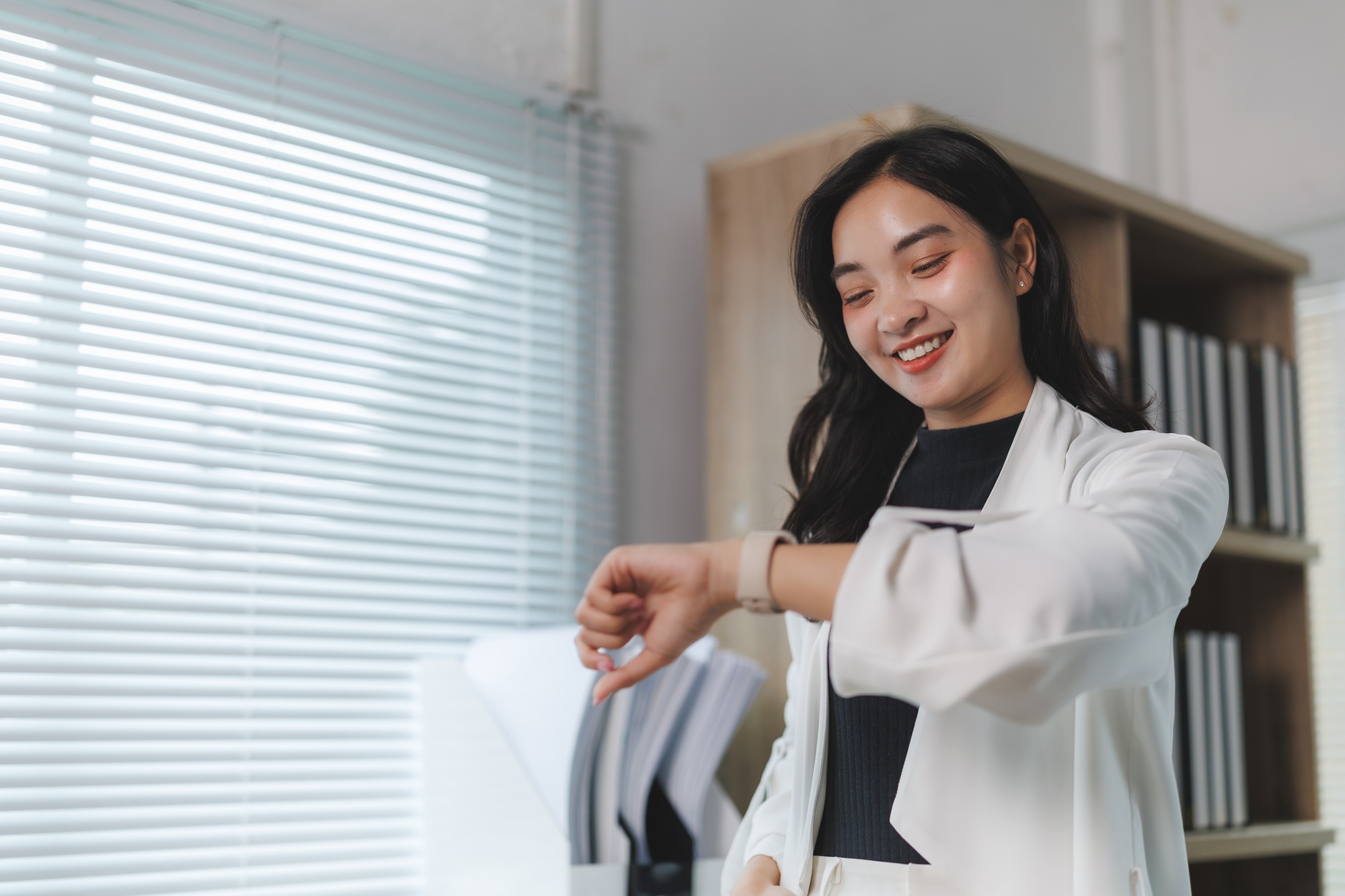 Smiling businesswoman checking time on smartwatch in modern office
